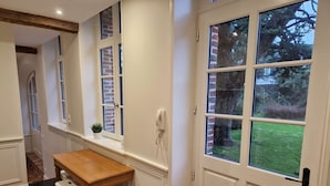 A kitchen with a wooden table and stools, a window with a view of greenery, and a white door. - Arras Quartier pr Fecture Familles Animaux (Arras)