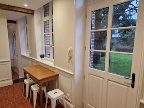 A kitchen with a wooden table and stools, a window with a view of greenery, and a white door. - Arras Quartier pr Fecture Familles Animaux (Arras)
