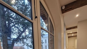 A hallway with a stone floor, a wooden staircase, and a view of a tree and building outside. - Arras Quartier pr Fecture Familles Animaux (Arras)