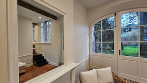 A room with a large mirror reflecting a staircase, a curved window with a view of greenery, and a wicker chair with cushions. - Arras Quartier pr Fecture Familles Animaux (Arras)