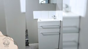 Une salle de bain avec un lavabo blanc, un miroir au-dessus et un mur recouvert de carreaux.