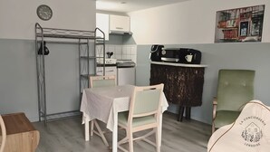 Une cuisine compacte avec un coin repas, une étagère en métal et une horloge au mur.