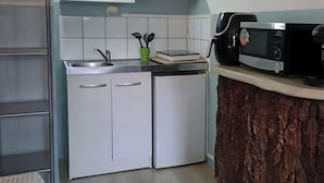 Une cuisine compacte avec des meubles blancs, un four à micro-ondes, une machine à café et un petit évier.