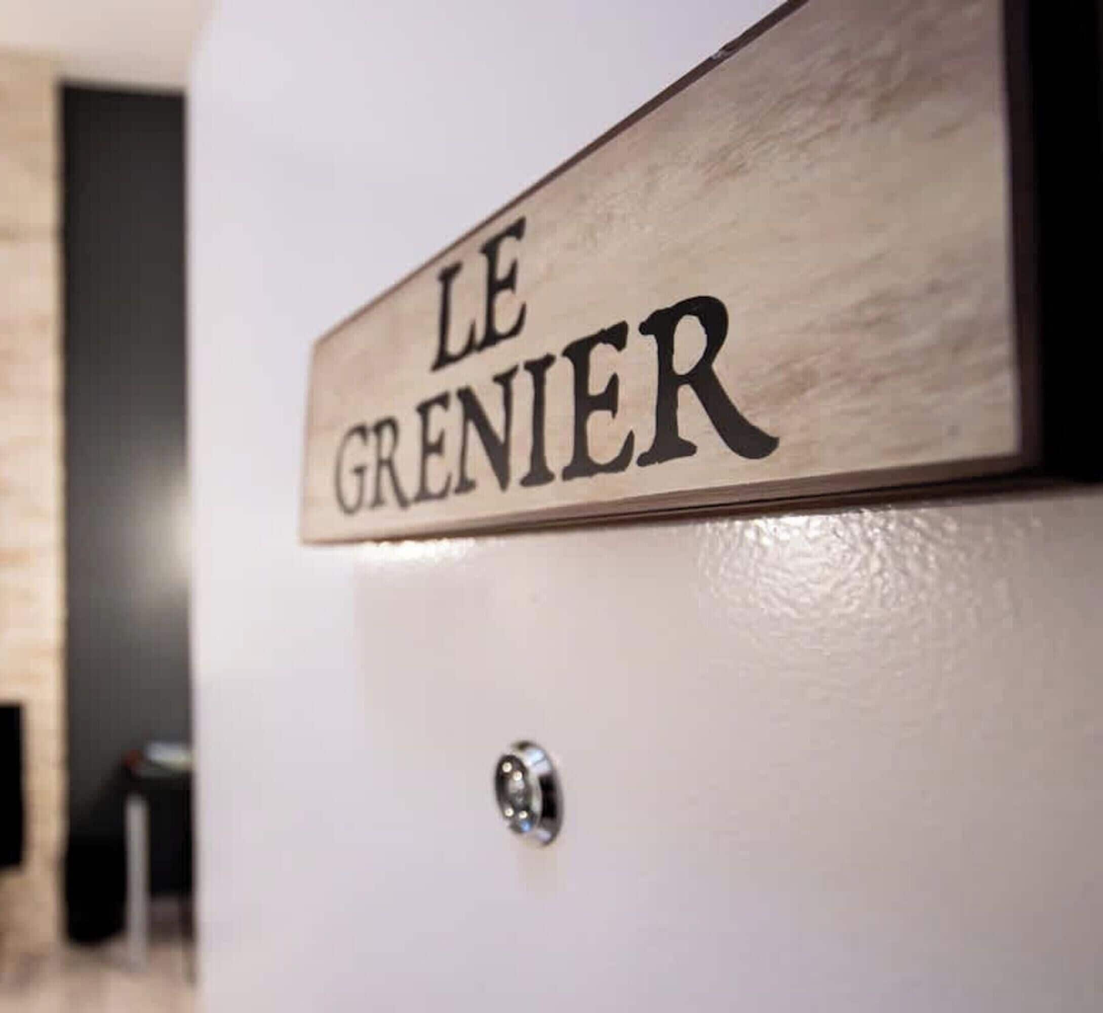 A wooden sign with the text 'LE GRENIER' on a white wall.