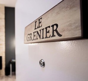 Ein hölzernes Schild mit dem Schriftzug 'LE GRENIER' an einer weißen Wand.