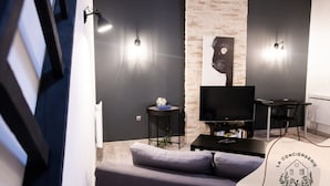 Un salon moderne doté d’un téléviseur à écran plat, d’un canapé, d’une petite table d’appoint et de deux lampes fixées au mur.