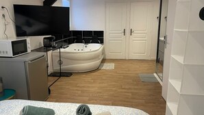 Una habitación de hotel moderna con cama, escritorio con computadora, televisor, bañera y armario.