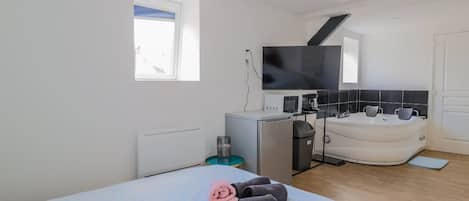 A hotel room with a bed, a TV, a small kitchenette, a bathtub, and a window.