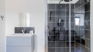 Un baño moderno con ducha de vidrio, tocador con espejo y un ventanal pequeño.