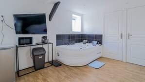 Un baño moderno con bañera, microondas, cafetera y televisor montado en la pared.