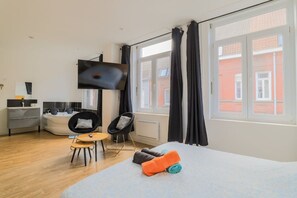 A modern hotel room with a bed, a TV, a small table, two chairs, a sofa, and a window with curtains. - Le Nid Cosy 2 Baln o et Wifi (Tourcoing)