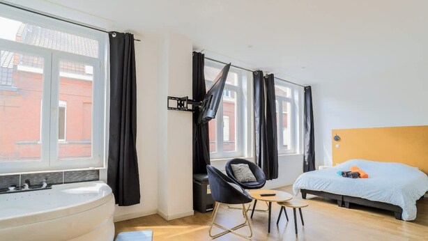 Ein modernes Schlafzimmer mit großem Fenster, einer Badewanne, einem Bett, einem Sessel und einem kleinen Tisch.