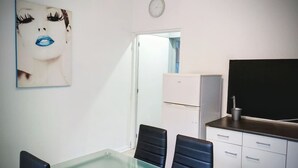 A room with a desk, two chairs, a white refrigerator, a flat-screen TV, and a wall clock. - Laverie de Fran ois Wifi Commerce 6pers Ar na (Lievin)