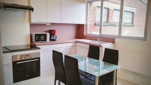 A compact kitchen with white cabinets, a microwave, a coffee maker, a dishwasher, and a glass-top dining table with four chairs. - Laverie de Fran ois Wifi Commerce 6pers Ar na (Lievin)