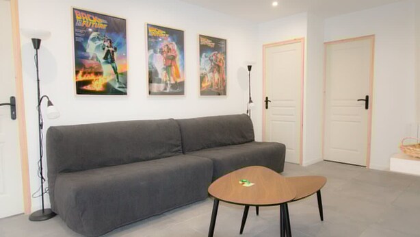 A modern room with a grey sofa, a small wooden table, and two posters on the wall. - Player 3 Wifi Jeux Parking Lave Linge 6 Pers (Noeux-les-Mines)