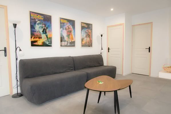 A modern room with a grey sofa, a small wooden table, and two posters on the wall. - Player 3 Wifi Jeux Parking Lave Linge 6 Pers (Noeux-les-Mines)