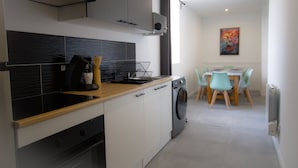 A modern kitchen with a built-in oven, a washing machine, and a dining area with a table and chairs. - Player 3 Wifi Jeux Parking Lave Linge 6 Pers (Noeux-les-Mines)