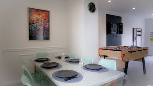 A dining area with a table set for four, a foosball table, a dartboard, and a clock on the wall. - Player 3 Wifi Jeux Parking Lave Linge 6 Pers (Noeux-les-Mines)
