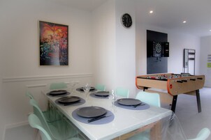Un comedor con una mesa dispuesta para cuatro personas, mesa de fútbol de mesa, dardo y un reloj en la pared.