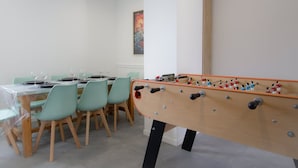 A room with a foosball table, a dining table with chairs, and a clock on the wall. - Player 3 Wifi Jeux Parking Lave Linge 6 Pers (Noeux-les-Mines)