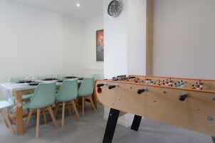 Una habitación con una mesa de fútbol, una mesa de comedor con sillas y un reloj en la pared.