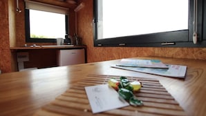 Ein Holztisch mit Papierkram und einer kleinen Pflanze, ein Fenster mit Blick und eine Küchenzeile mit Spüle und Schränken.
