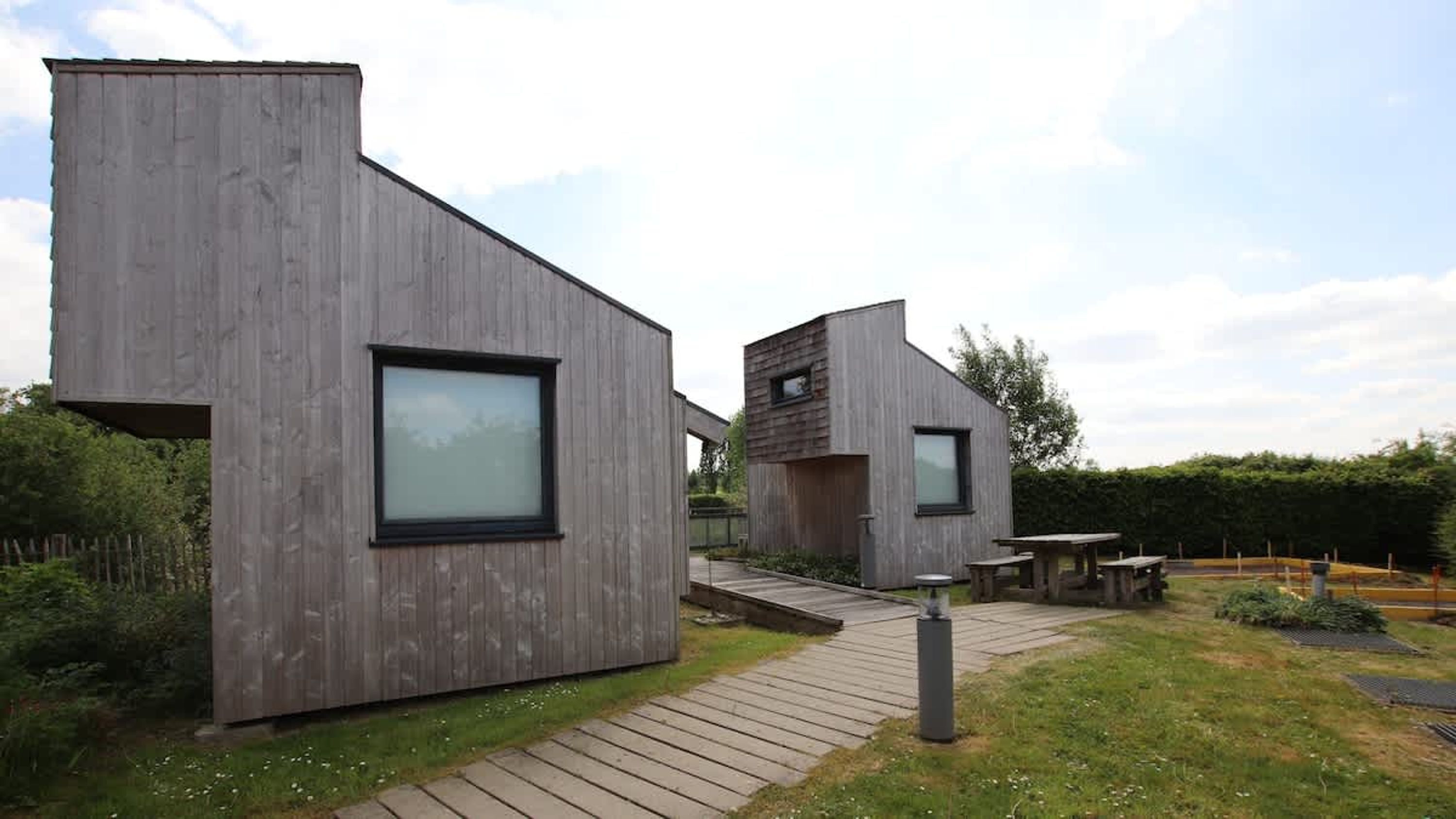 Una casa moderna con fachada de madera, un ventanal grande y un pequeño patio.