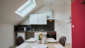 A modern kitchen with a skylight, white cabinets, and a dining area set for two with a table and chairs. - En d Placement 9 Dernier Tage Wifi Gratuit (Tourcoing)