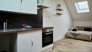 A compact kitchen with a built-in oven, a small window, and a loft-style bedroom with a bed and a window. - En d Placement 9 Dernier Tage Wifi Gratuit (Tourcoing)