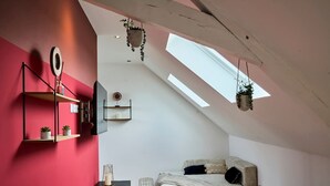 A bedroom with a sloped ceiling, skylights, a bed, a bedside table, a small shelf with plants, and a mirror. - En d Placement 9 Dernier Tage Wifi Gratuit (Tourcoing)