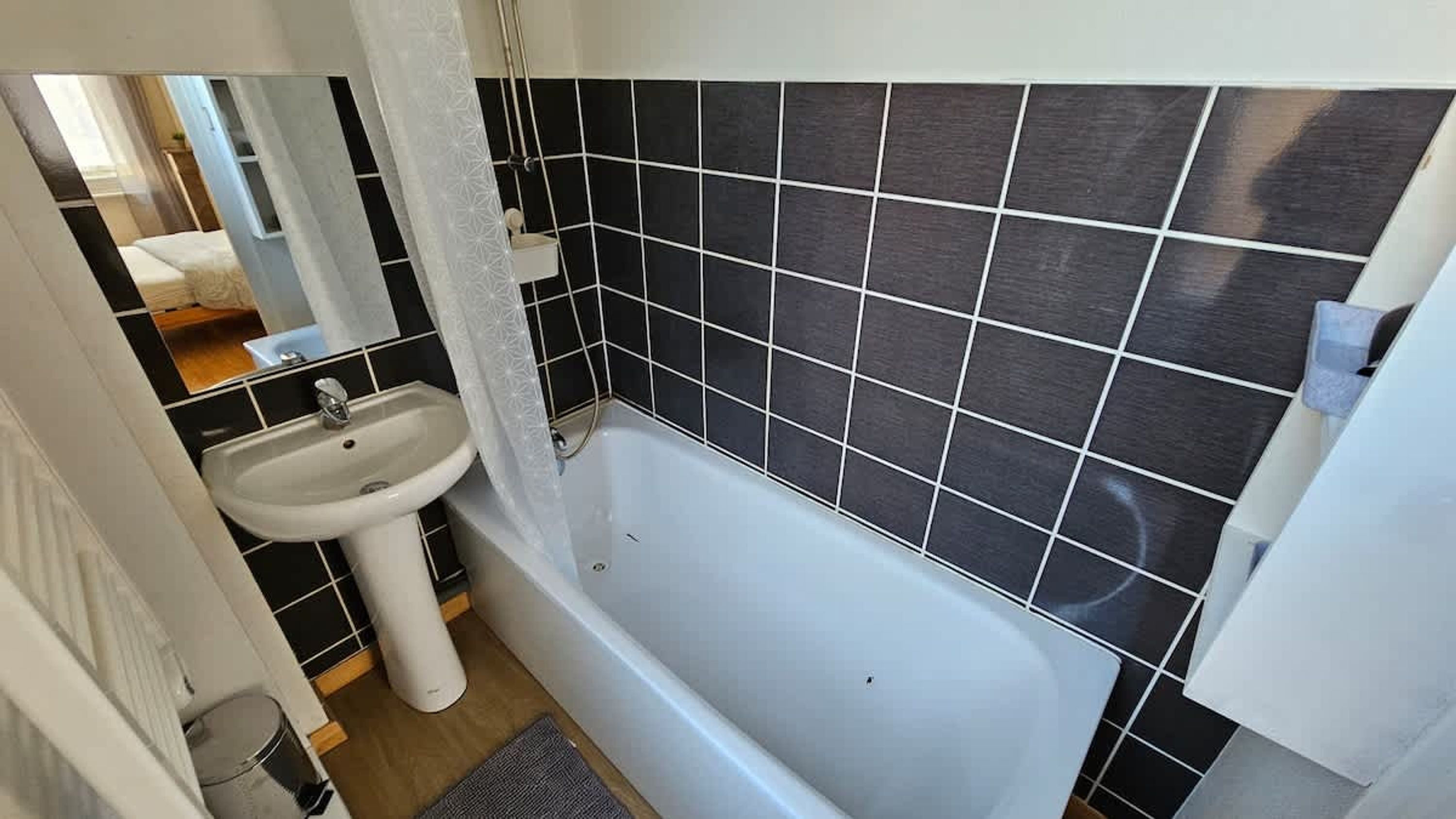 A bathroom with a bathtub, a sink, and black tiled walls.