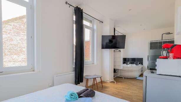 Une chambre d’hôtel moderne équipée d’un lit, d’une télévision, d’une salle de bain avec baignoire et d’une petite table.