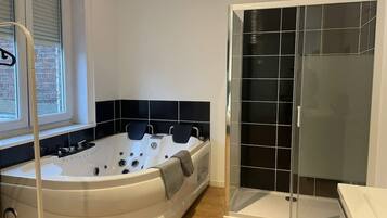 Un baño con una bañera blanca, ducha con mampara de vidrio y ventana con persianas.