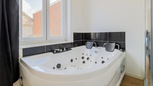 Une salle de bain moderne avec une grande baignoire, une fenêtre et des murs recouverts de carreaux noirs.