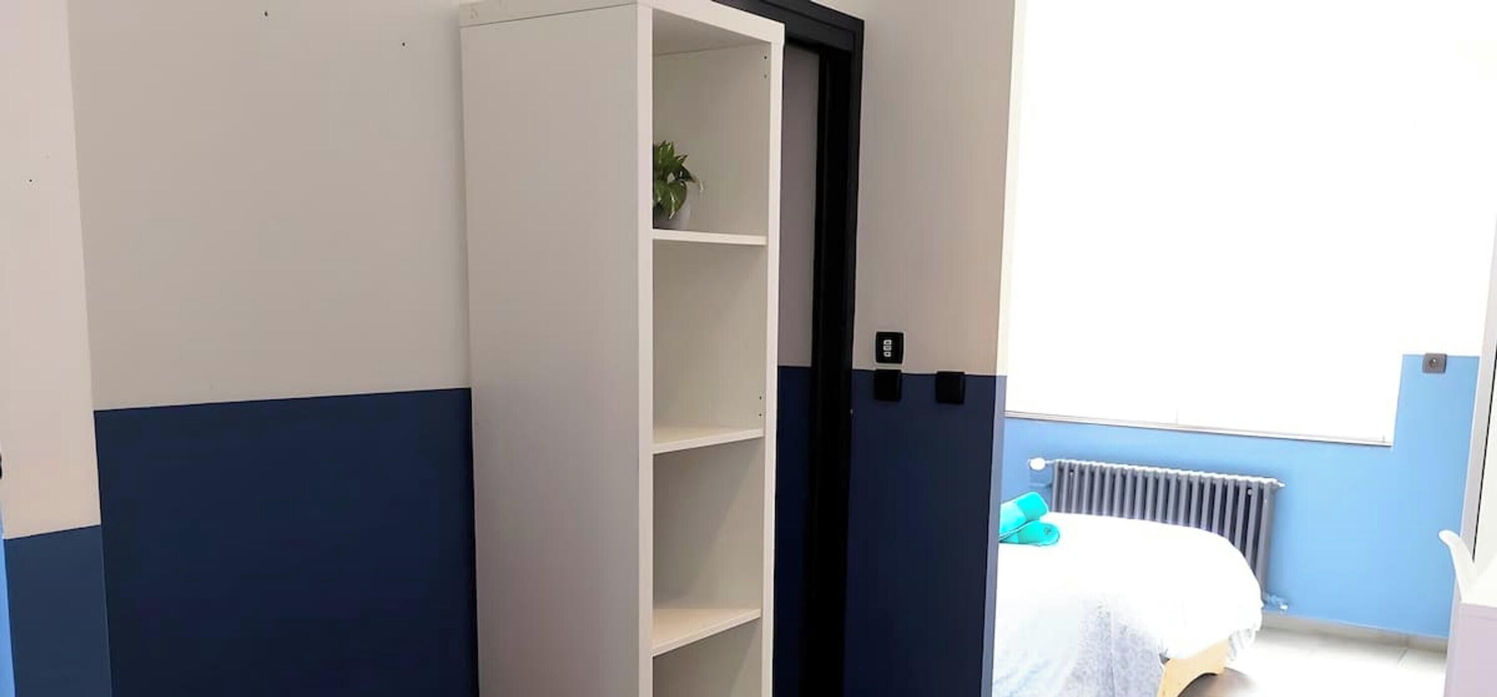 A room with a bed, a radiator, a potted plant, and a door leading to another room.