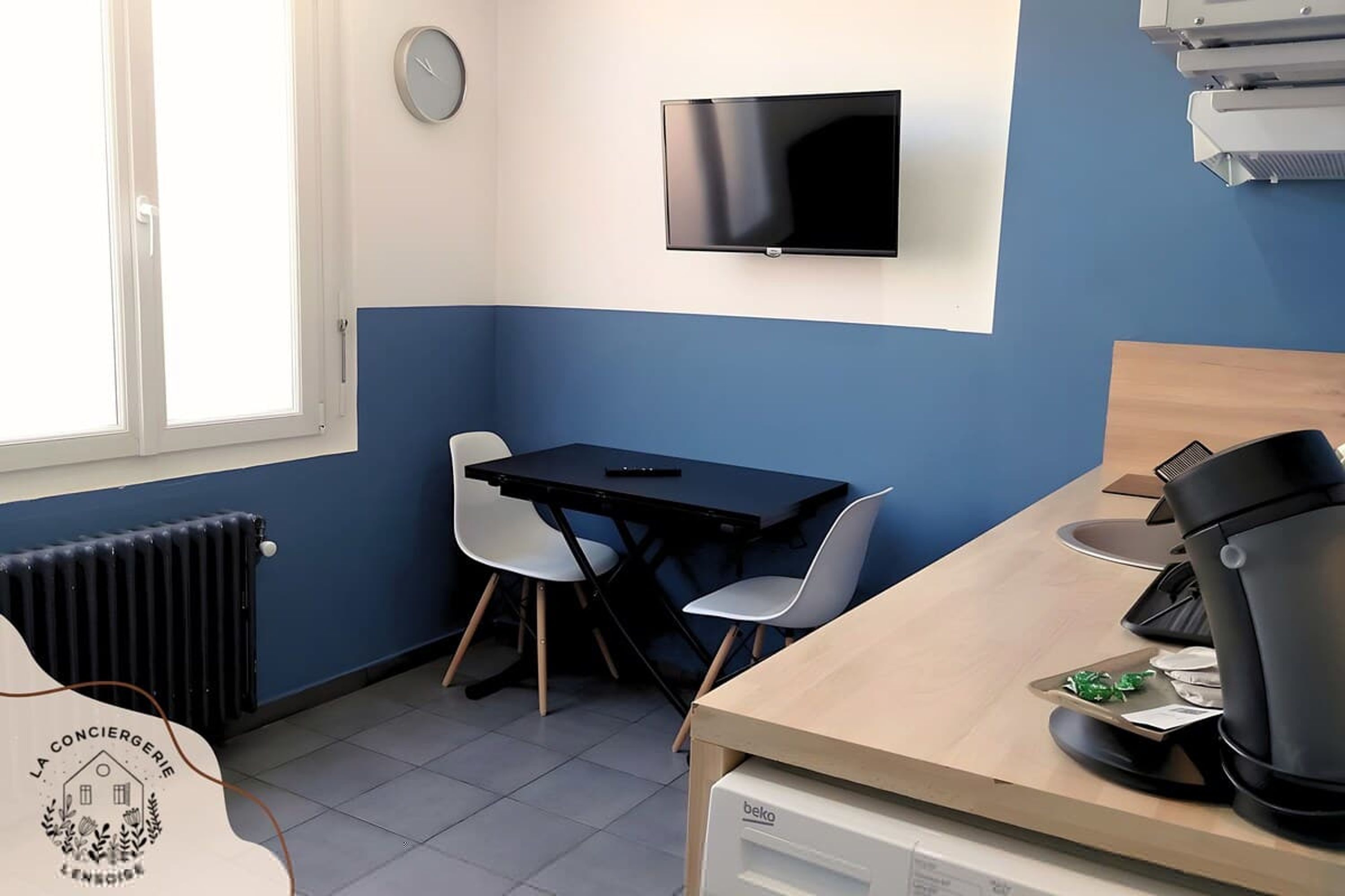 Una habitación pequeña con cama, escritorio, silla, televisor, radiador y ventana.