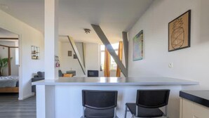 Een moderne keuken met een centraal eiland, twee zwarte stoelen, en een eethoek met uitzicht op het buitenland.