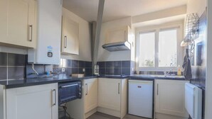 Een compacte keuken met een ingebouwde oven, een vaatwasser en een raam dat natuurlijk licht binnenlaat.