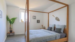 Een hemelbed met een grijze sprei, een potplant en een decoratief object aan de muur.