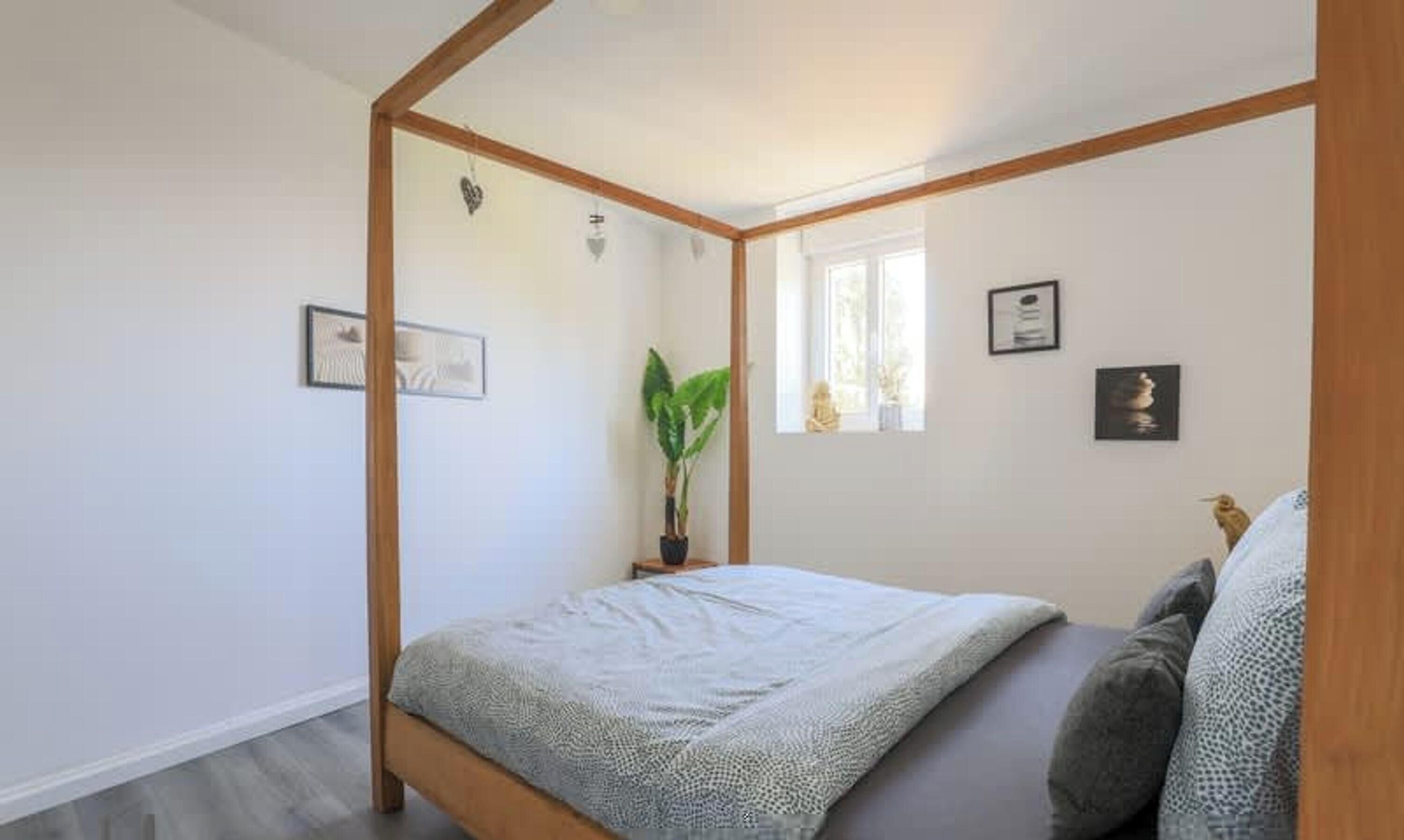Ein Schlafzimmer mit Bett, Fenster, Pflanze und Wandbildern.