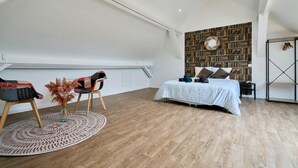 A bedroom with a loft-style ceiling, a bed with a patterned bedspread, a bookshelf, and a circular rug. - Le Grand Duplex Balneo 10 Minutes de la Gare (Tourcoing)