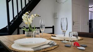 A dining table set with plates, cutlery, and glasses, with a staircase and a door in the background. - Le Grand Duplex Balneo 10 Minutes de la Gare (Tourcoing)