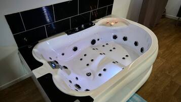 Un bain à remous blanc doté de plusieurs jets, d’un panneau de commande et, en arrière-plan, d’un mur recouvert de carreaux noirs.
