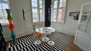 Ein modernes Zimmer mit einem runden Tisch, zwei Stühlen, einem schwarz-weißen Teppich und einem Fenster mit Blick auf Gebäude.