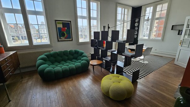 Ein modernes Wohnzimmer mit einem grünen Sofa, einem gelben Pouf und einem schwarz-weißen StreifenTeppich.