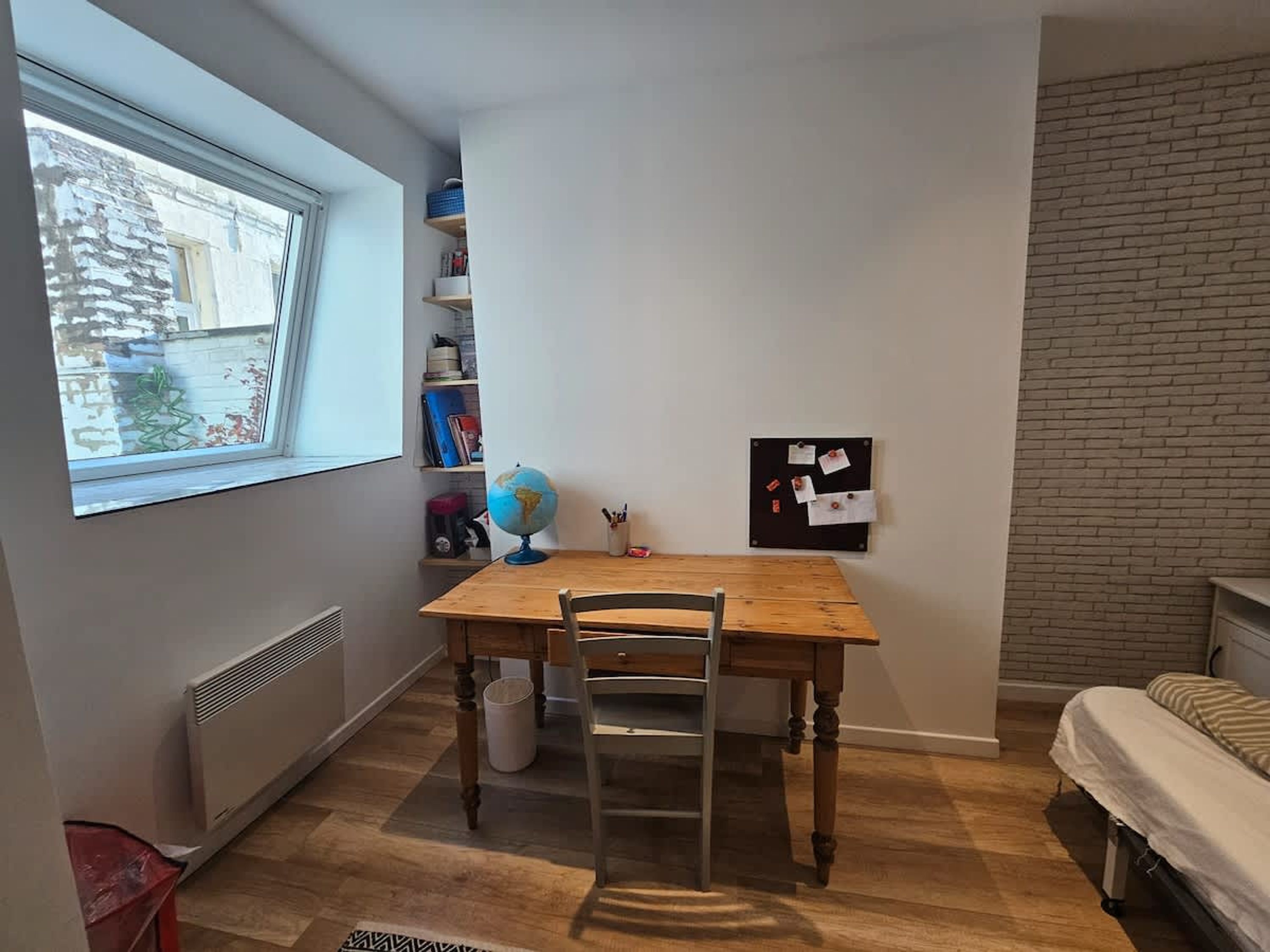 A room with a wooden table, a chair, a globe, a bulletin board, and a window.
