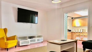 A modern living room with a flat-screen TV, a yellow armchair, a green sofa, a white coffee table, and a kitchen area visible through an open door. - Grande Maison 17 Personnes (Arras)