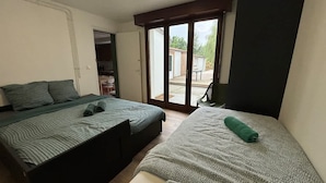 A bedroom with two beds, a sliding glass door to a patio, and a small desk area. - Grande Maison 17 Personnes (Arras)