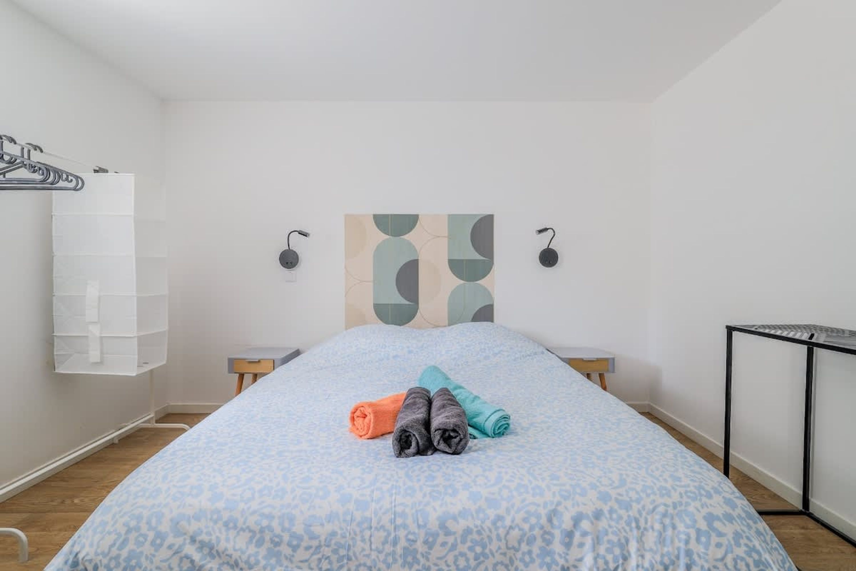 Un dormitorio con una cama, una mesita de noche, un estante en la pared y una obra de arte abstracta en la pared.