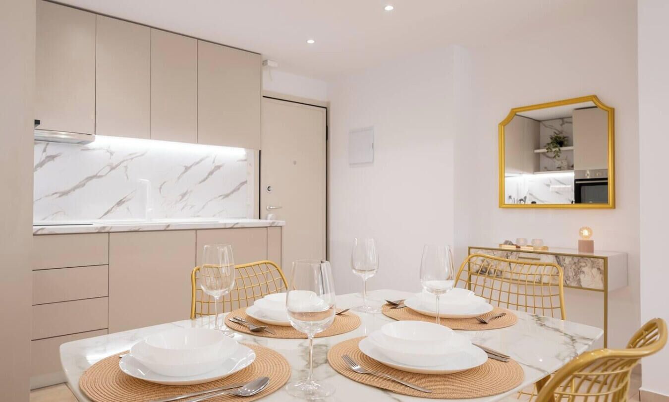 A dining area with a marble countertop, gold chairs, and a mirror on the wall.
